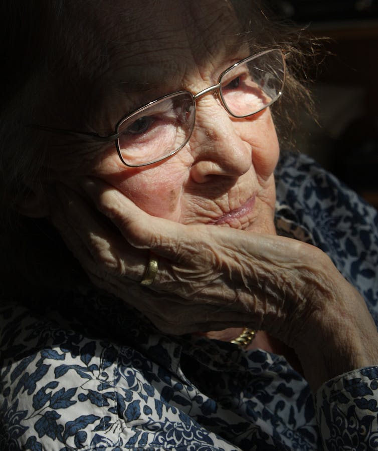 An older woman looks out the window.